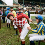 A jockey bent over whipping himself with a horse whip